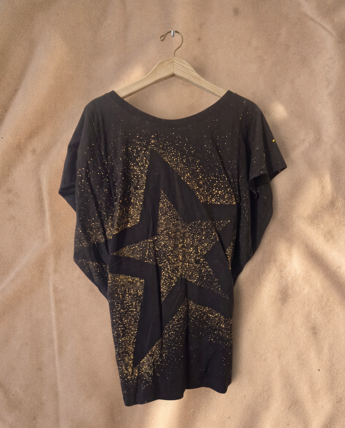 Valentina Dreamcatcher top in zwart met een grote gouden sterrenprint en spikkelpatroon op een houten hanger