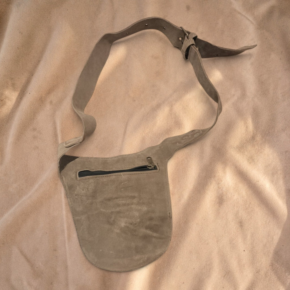 Valentina Wild Path taupe suede fanny pack with adjustable strap and zippered pocket on a neutral fabric background