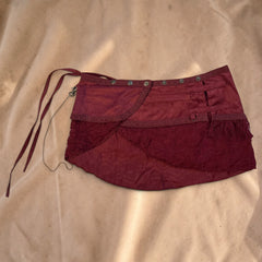 Valentina burgundy mini skirt with intricate lace trim, metallic studs, and a delicate chain detail on a light floor.