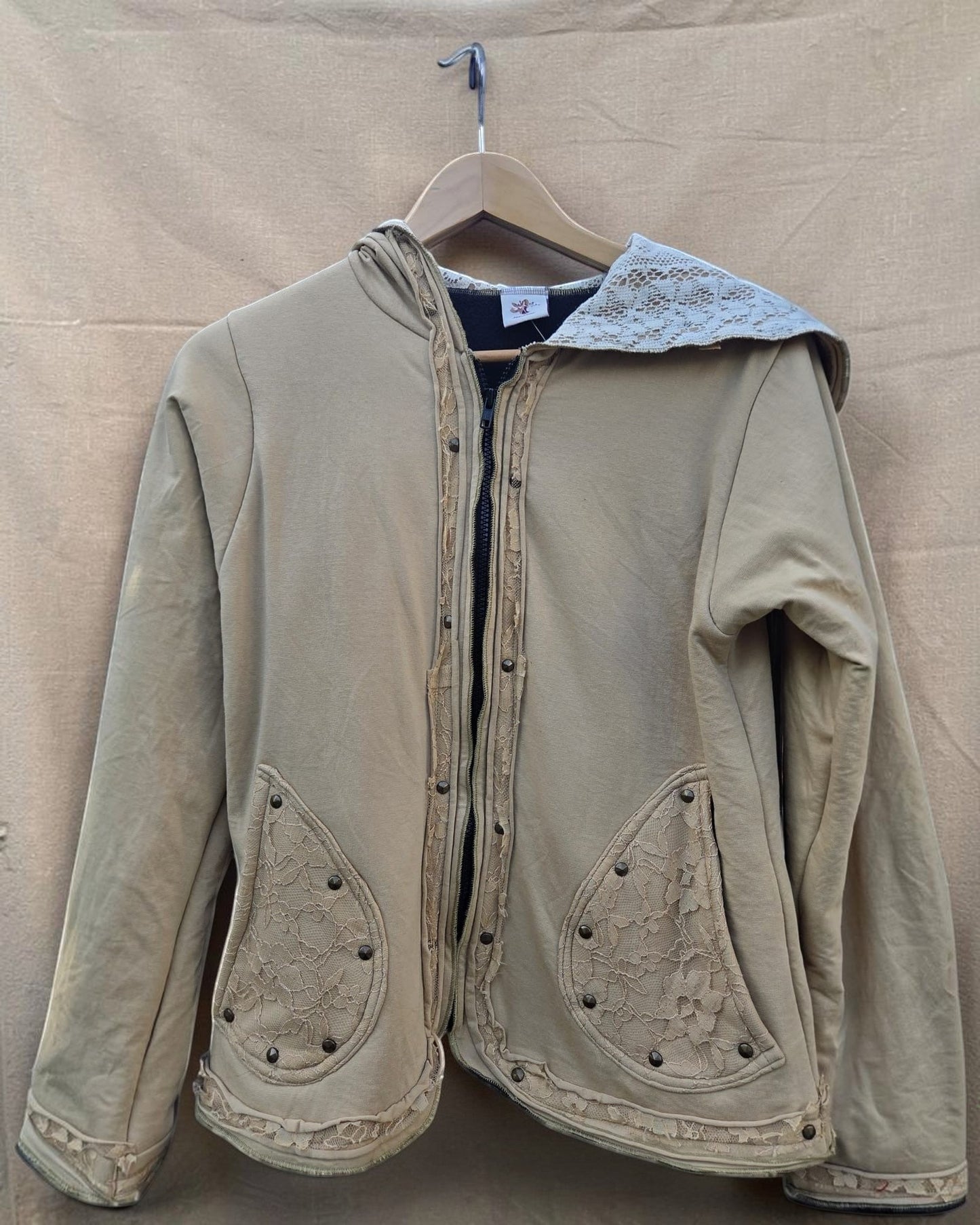 Valentina dames hoodie in beige met kanten details en knopen. Capuchon, zakken en zoom zijn versierd met kant.