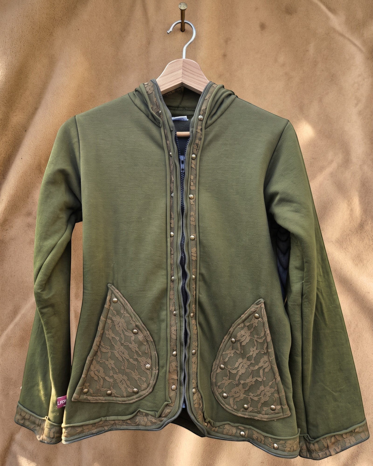 Valentina Soft Nomad jack in olijfgroen met kanten details, capuchon en drukknopen op een houten kledinghanger.